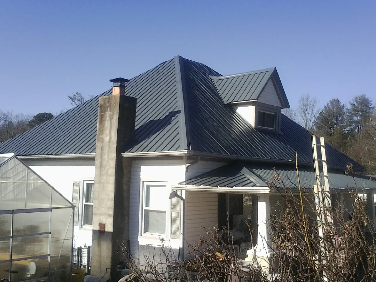 Dark blue standing seam metal roof on a white farmhouse with dormer — Slate & Tile Roof Repair by Roofing Brothers in Belle Center