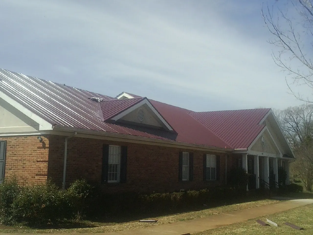 Red metal roof with gabled entries on a long brick building, from a Hail Damage Roof Repair job in Belle Center