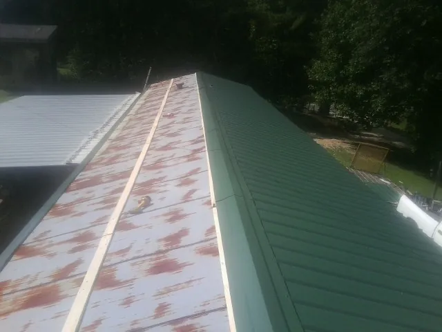 Old rusted panels beside newly installed green metal roofing — Wind Damage Roof Repair by Roofing Brothers in Belle Center