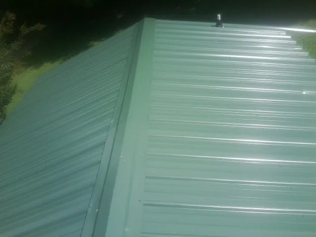 New green metal panels meeting at the ridge of a roof — Flat Roof Repair work by our crew in Belle Center
