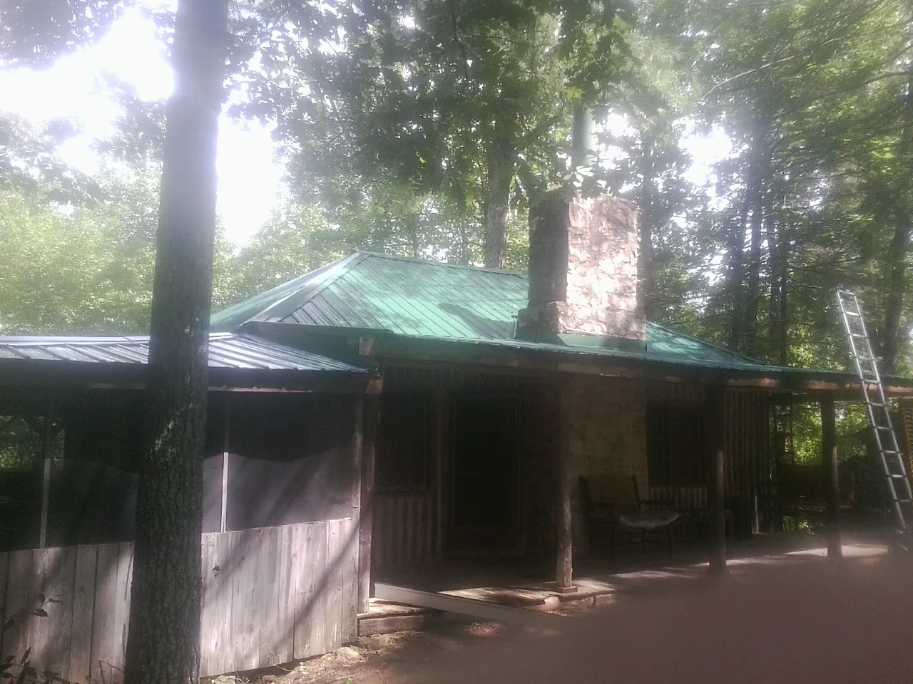 Green metal roof and stone chimney above a log cabin porch in Belle Center
