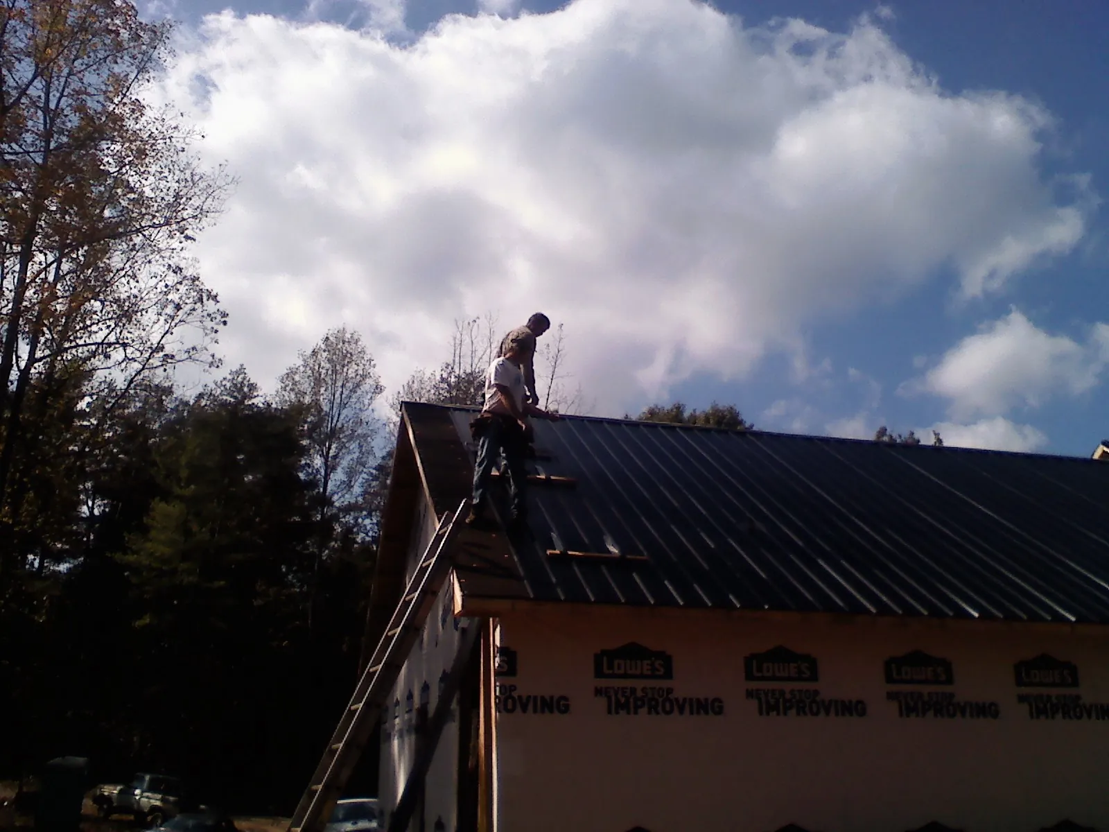 Roofer fastening dark metal panels high against a cloudy sky, from a Roof Inspection job in Belle Center