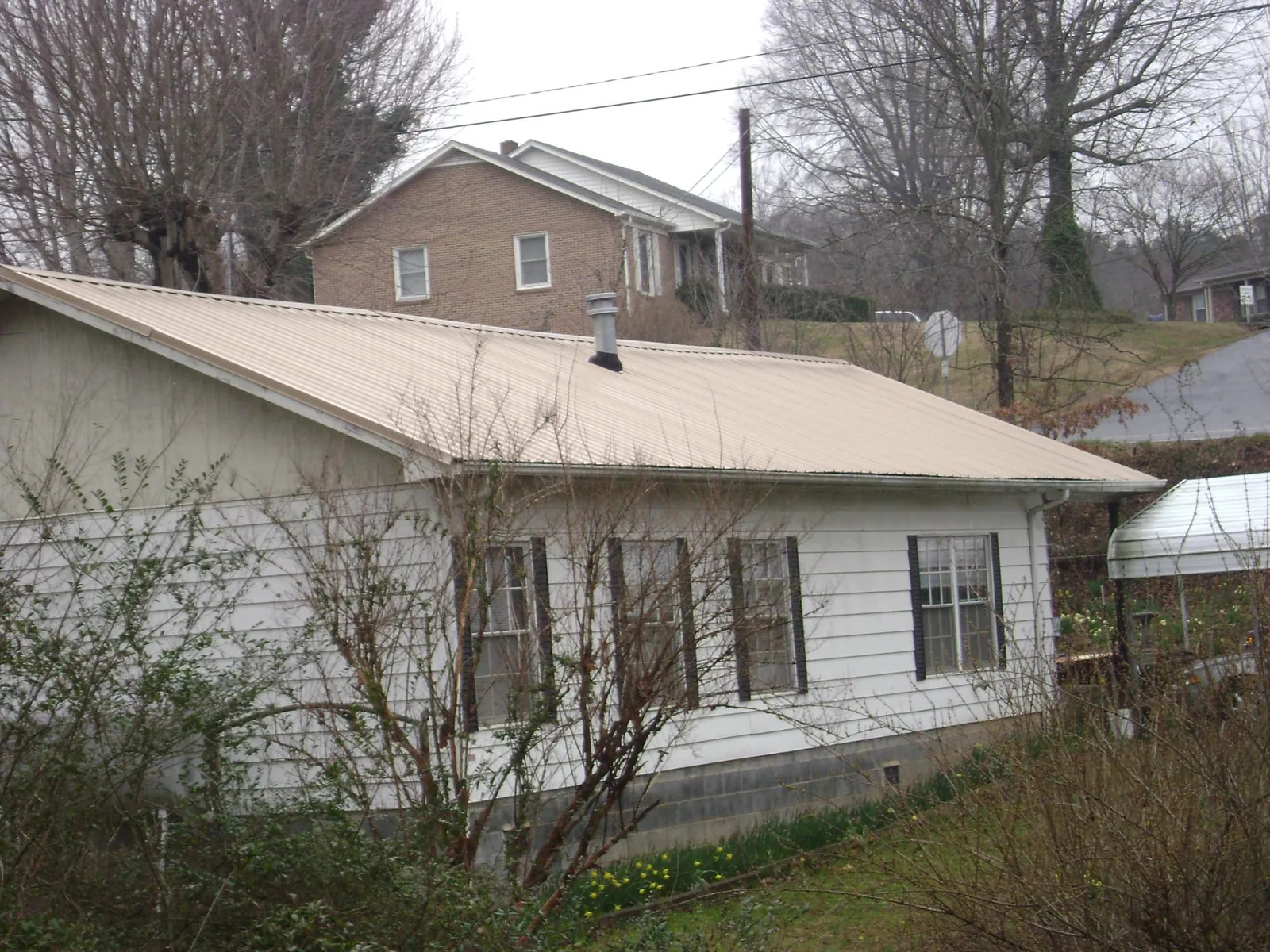 Tan metal roof on a white sided house set into a hillside — Commercial Roofing by Roofing Brothers in Belle Center
