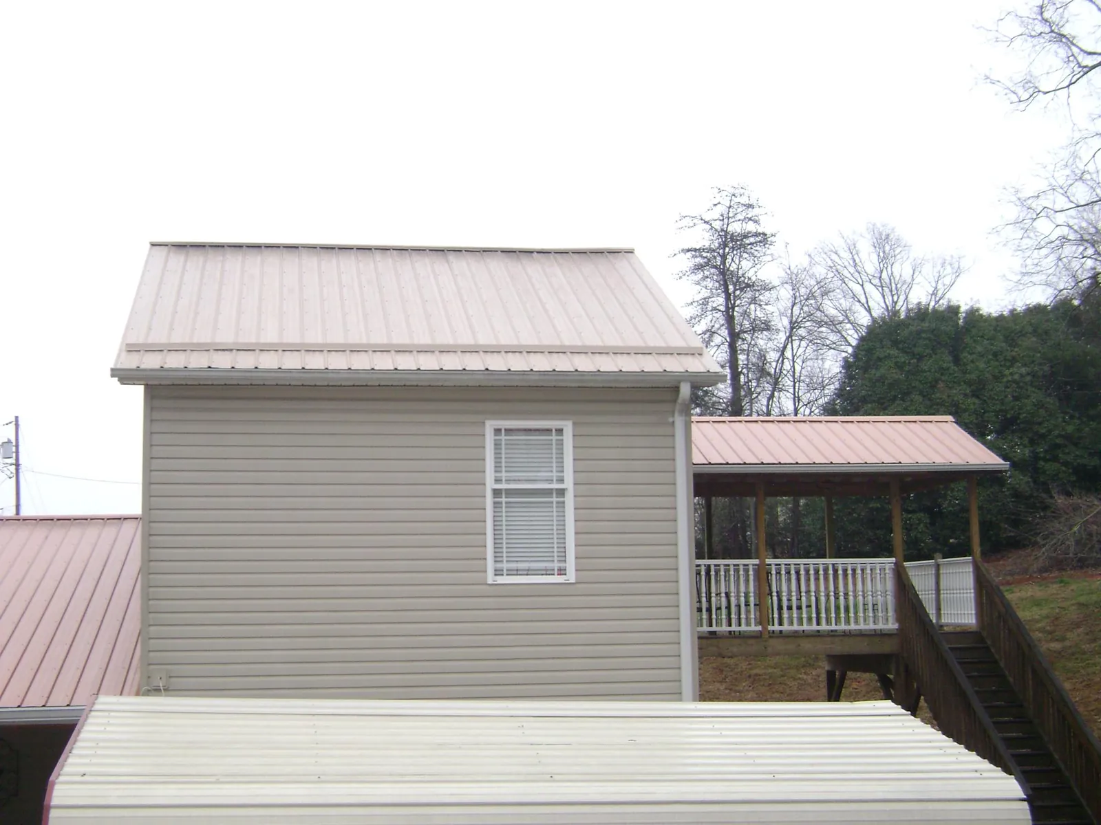 Tan metal roofs on a two story addition and attached porch, from a Roof Replacement job in Belle Center